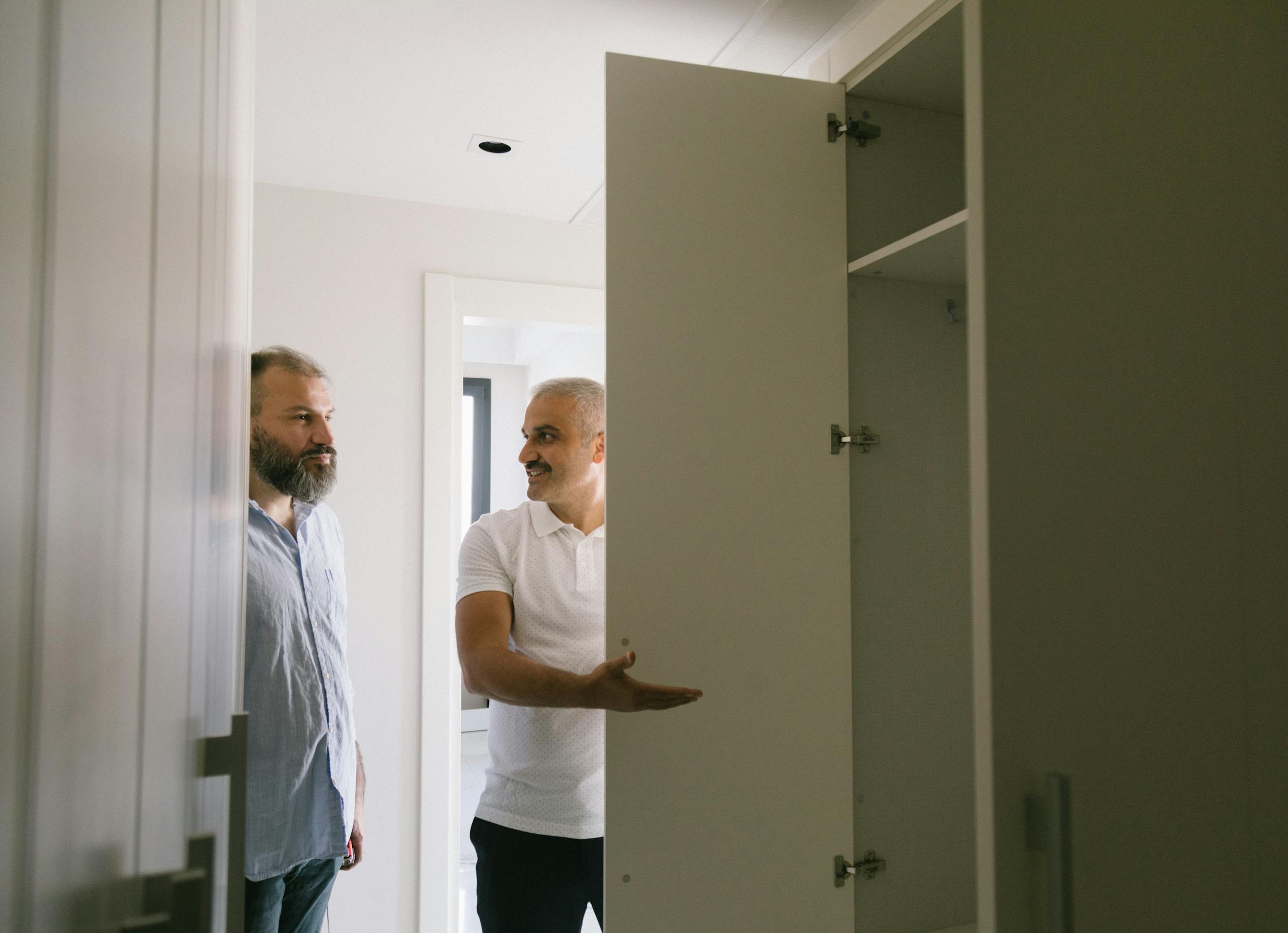 Man in White Polo Shirt Showing the Closet to a Man in Gray Shirt